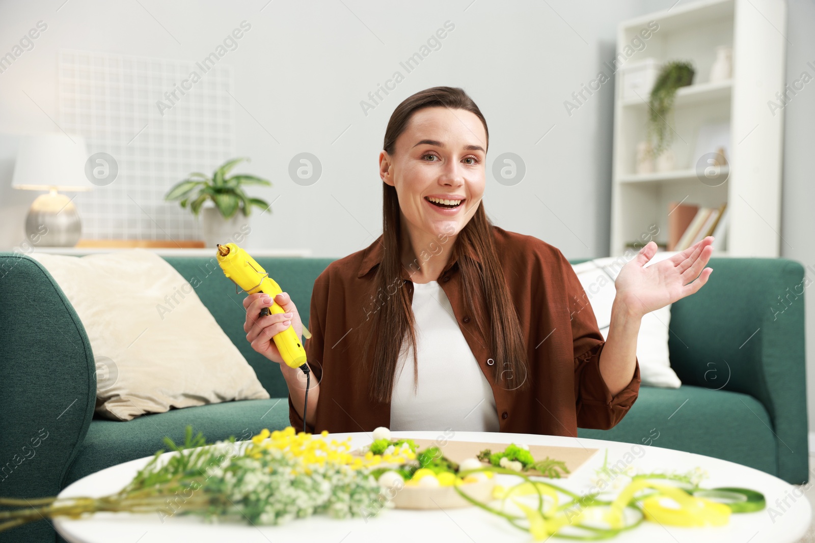 Photo of Woman with hot glue gun making craft at table indoors