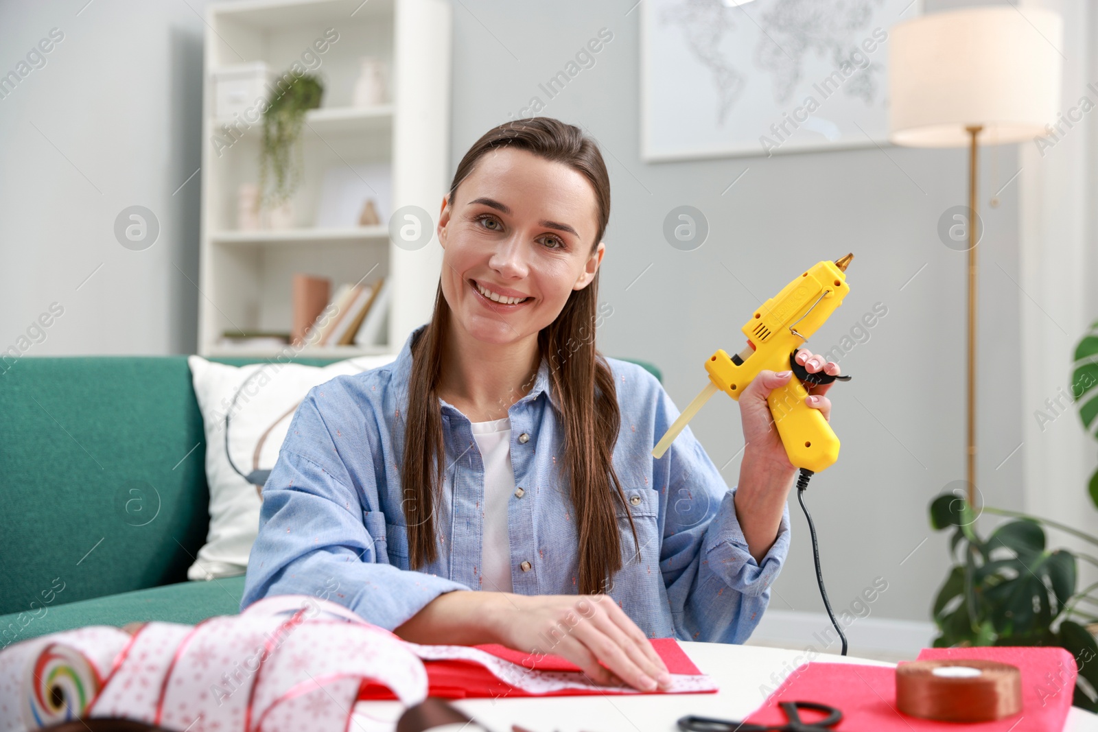 Photo of Woman with hot glue gun at table indoors