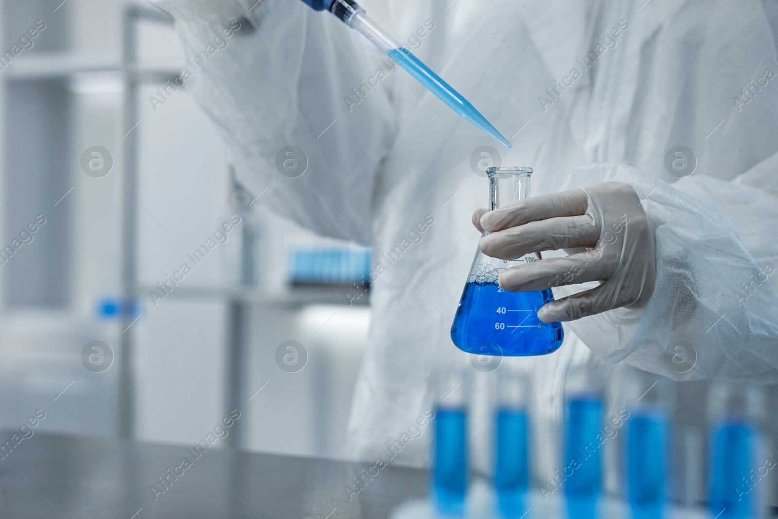 Photo of Scientist dripping blue sample into flask in laboratory, closeup