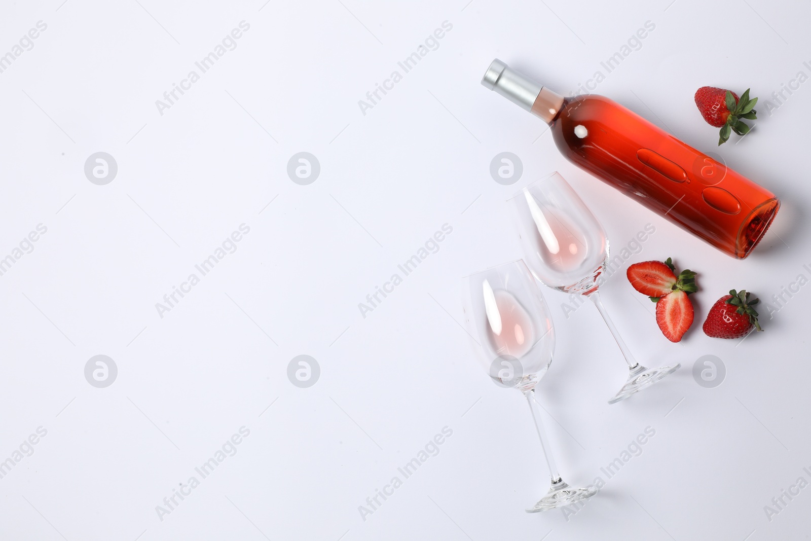 Photo of Bottle of rose wine, glasses and strawberries on white background, flat lay. Space for text