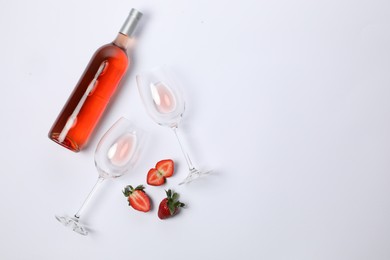 Bottle of delicious rose wine, glasses and strawberries on white background, flat lay. Space for text