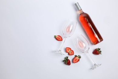 Bottle of delicious rose wine, glasses and strawberries on white background, flat lay. Space for text