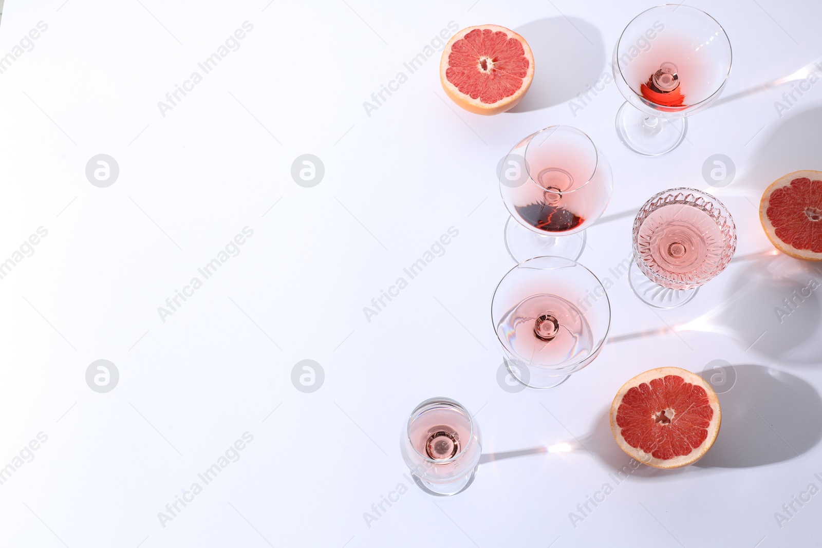 Photo of Tasty rose wine in glasses and fresh grapefruits on white background, above view. Space for text