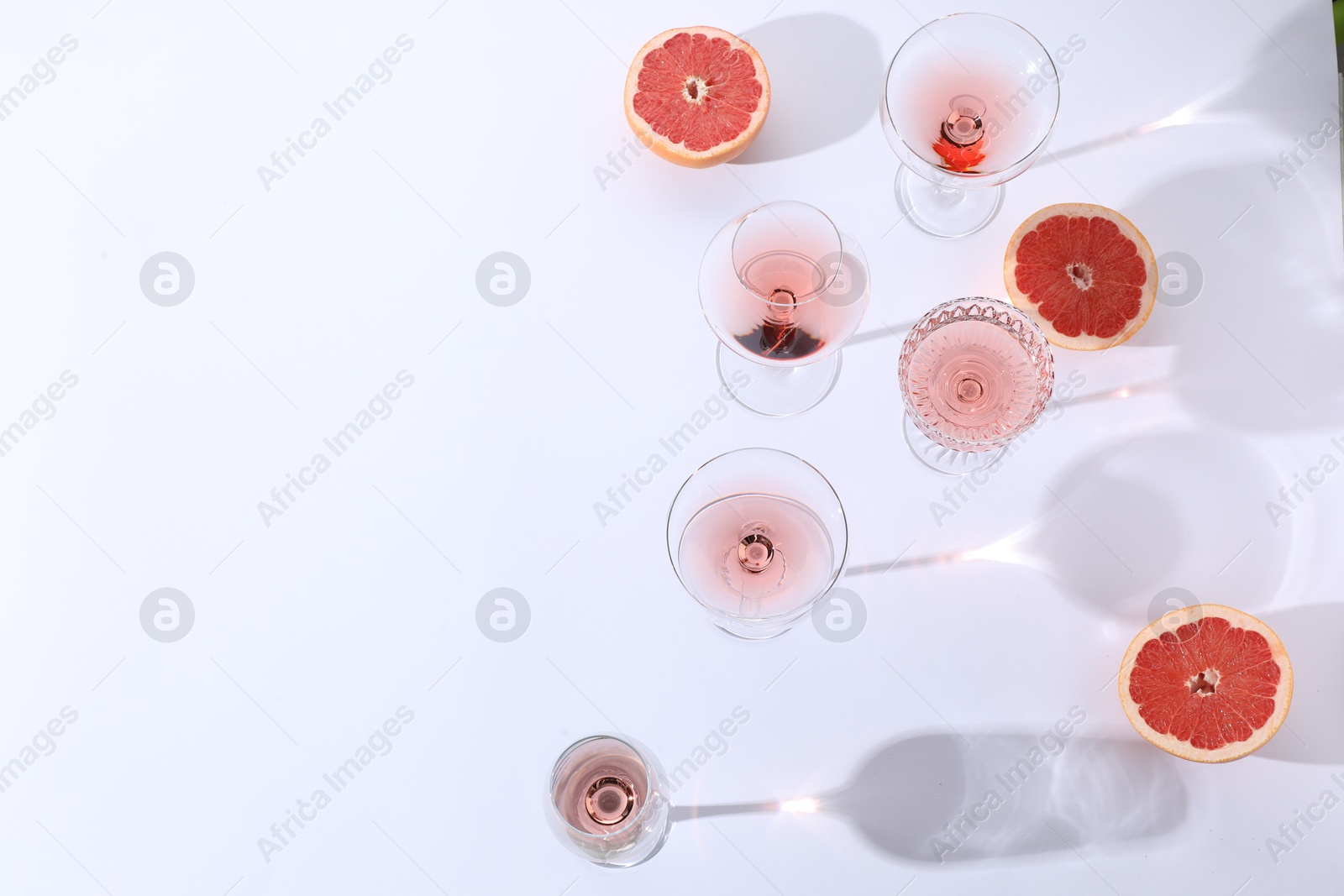 Photo of Tasty rose wine in glasses and fresh grapefruits on white background, above view. Space for text