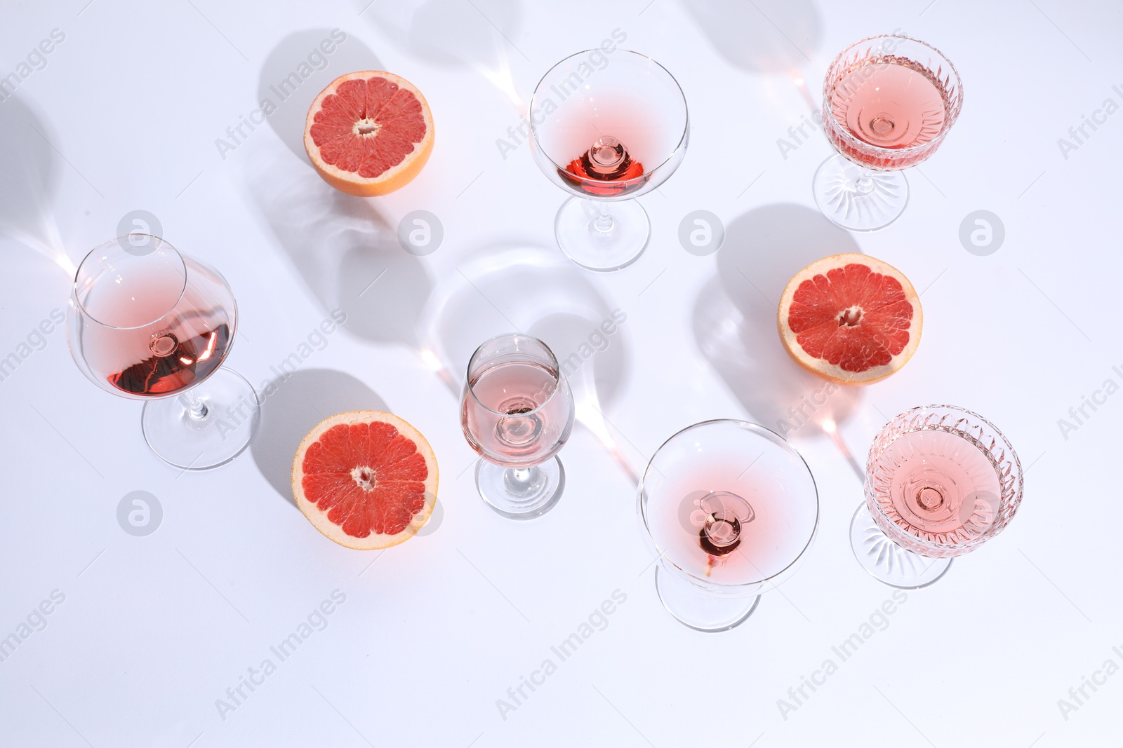 Photo of Tasty rose wine in glasses and fresh grapefruits on white background, above view