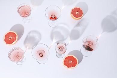 Tasty rose wine in glasses and fresh grapefruits on white background, above view