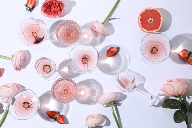 Flat lay composition with rose wine in glasses and flowers on white background