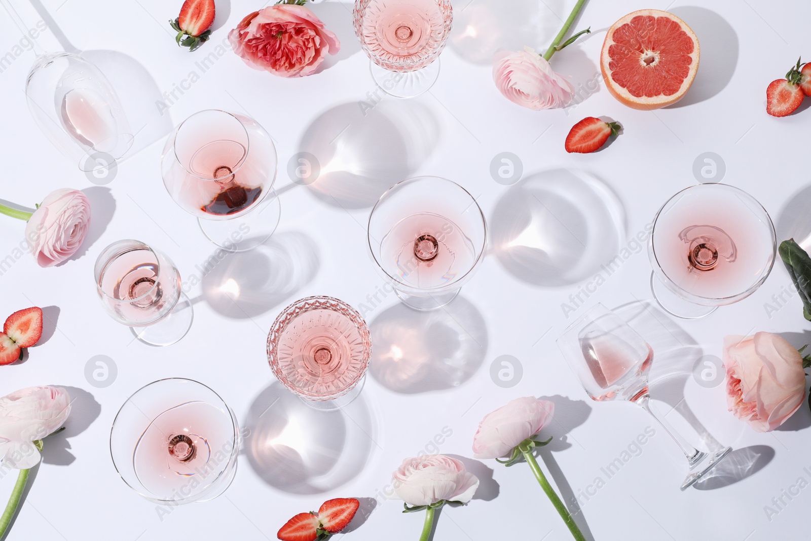 Photo of Flat lay composition with rose wine in glasses and flowers on white background