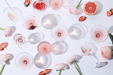 Flat lay composition with rose wine in glasses and flowers on white background