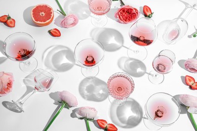 Photo of Composition with rose wine in glasses, flowers and strawberries on white background, above view