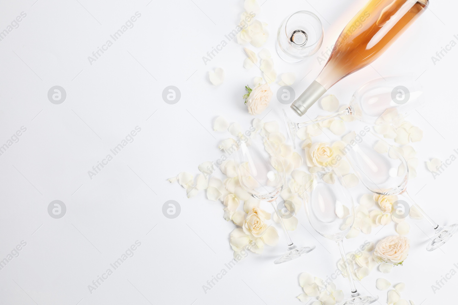 Photo of Flat lay composition with rose wine, glasses and petals on white background. Space for text