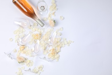 Photo of Flat lay composition with rose wine, glasses and petals on white background. Space for text