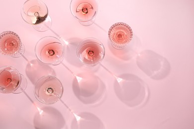 Tasty rose wine in glasses on pink background, flat lay. Space for text