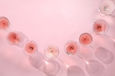 Photo of Tasty rose wine in glasses on pink background, flat lay. Space for text