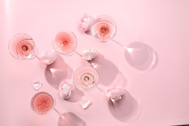 Tasty rose wine in glasses and beautiful flowers on pink background, flat lay