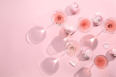 Photo of Tasty rose wine in glasses and beautiful flowers on pink background, flat lay. Space for text