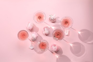 Tasty rose wine in glasses and beautiful flowers on pink background, flat lay