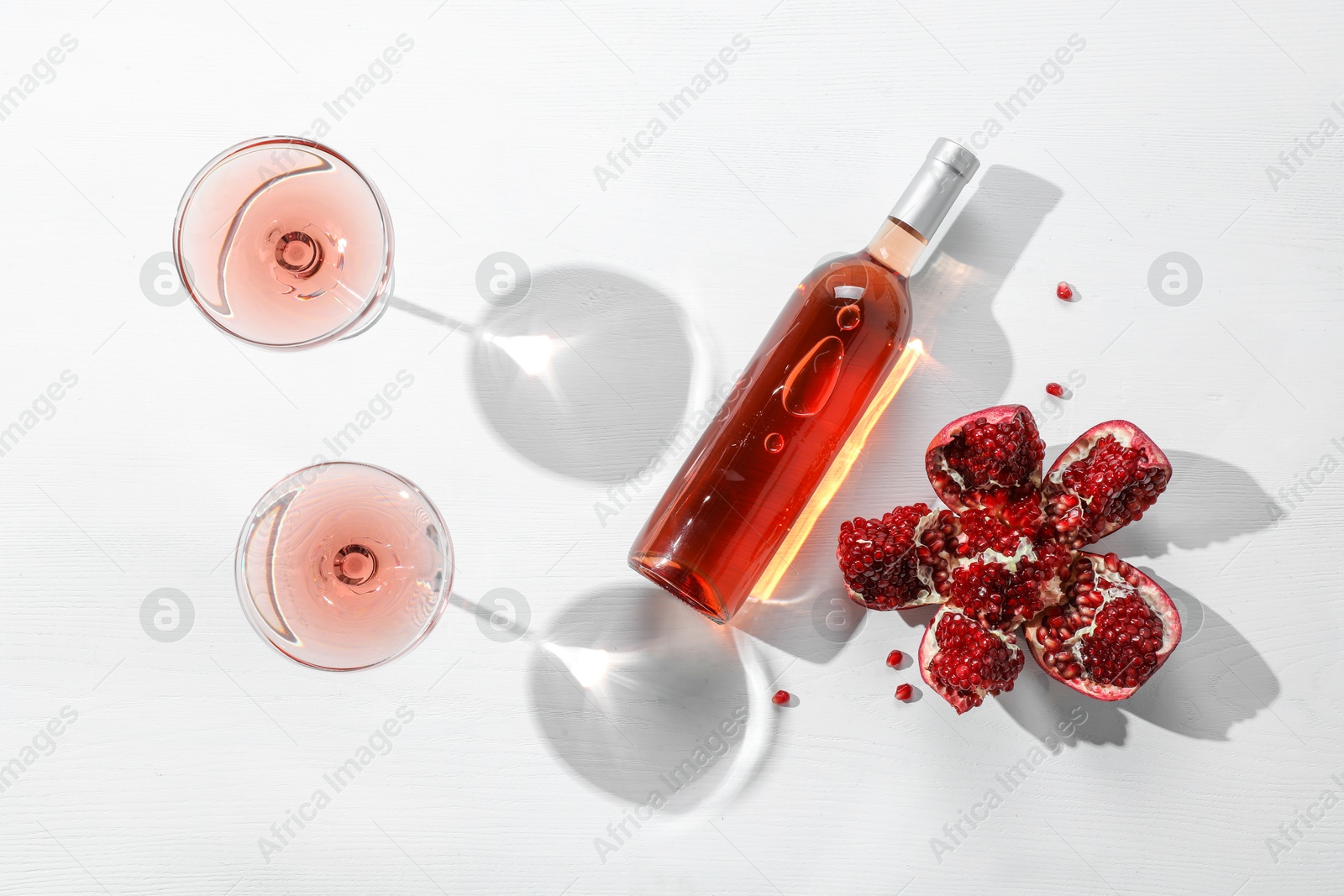 Photo of Delicious rose wine and fresh pomegranate on white table, flat lay