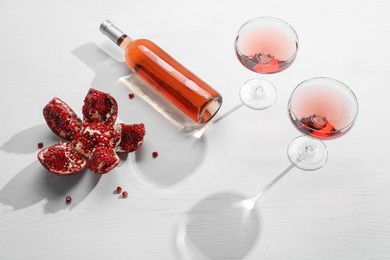 Photo of Delicious rose wine and fresh pomegranate on white wooden table