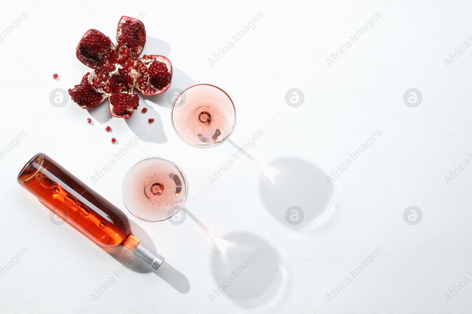 Photo of Delicious rose wine and fresh pomegranate on white table, flat lay. Space for text