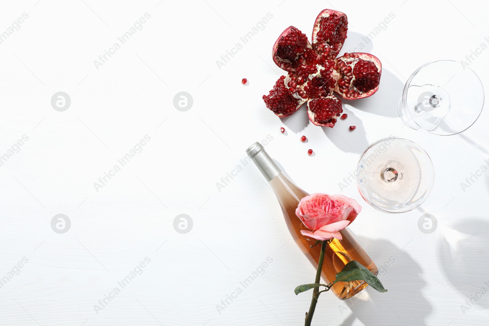 Photo of Flat lay composition with delicious rose wine and pomegranate on white background. Space for text