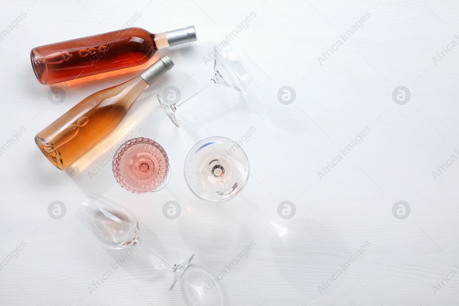 Photo of Bottles of delicious rose wine and glasses on white wooden table, flat lay. Space for text