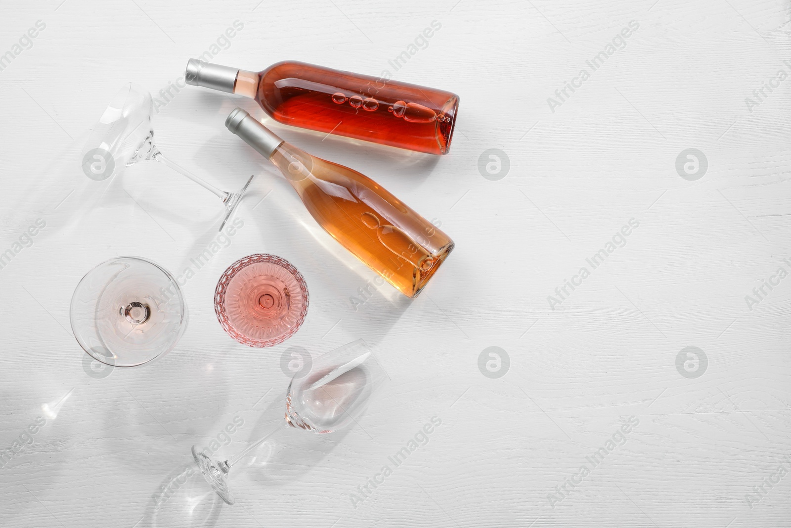 Photo of Bottles of delicious rose wine and glasses on white wooden table, flat lay. Space for text