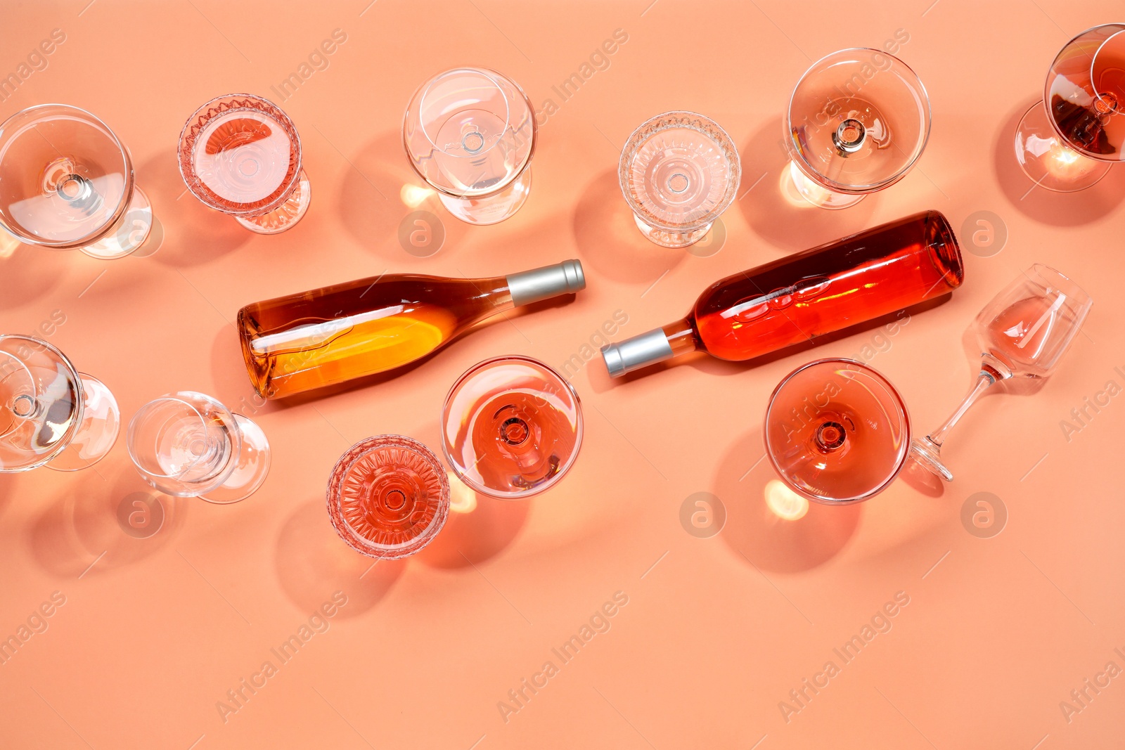 Photo of Delicious rose wine in glasses and bottles on coral background, flat lay