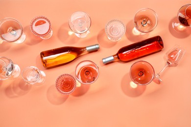 Photo of Delicious rose wine in glasses and bottles on coral background, flat lay