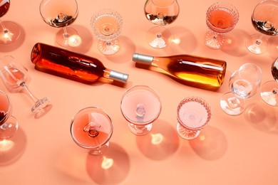 Delicious rose wine in glasses and bottles on coral background, above view