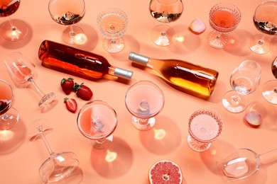 Composition with delicious rose wine in glasses and bottles on coral color background, above view