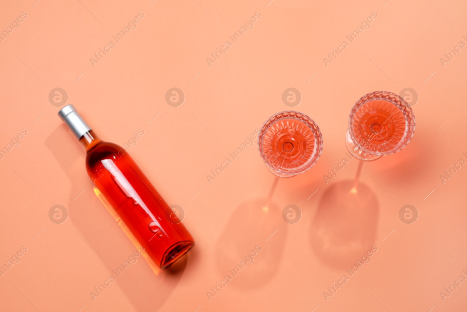 Photo of Delicious rose wine in glasses and bottle on coral color background, flat lay