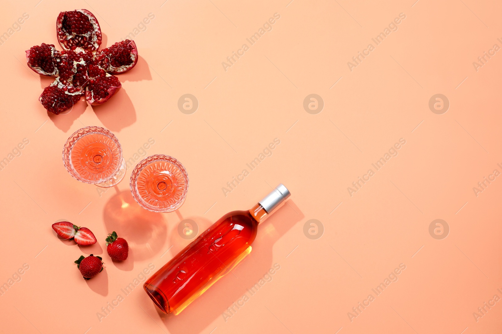 Photo of Tasty rose wine, pomegranate and strawberries on coral color background, flat lay. Space for text