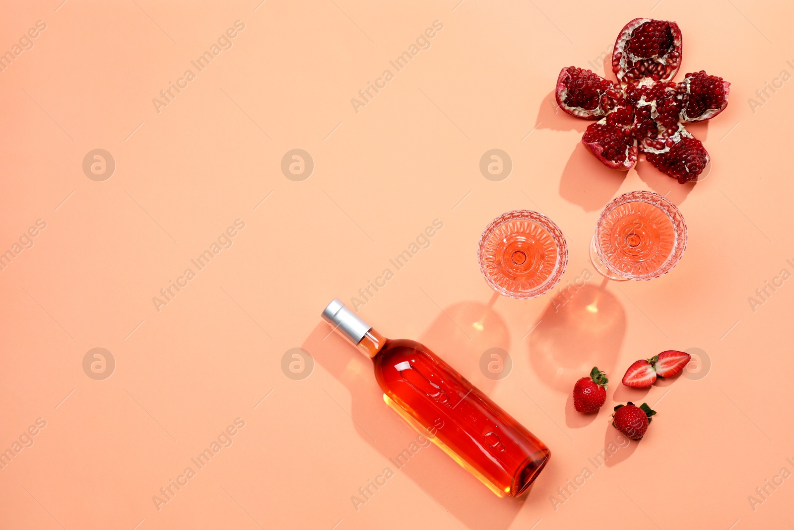 Photo of Tasty rose wine, pomegranate and strawberries on coral color background, flat lay. Space for text