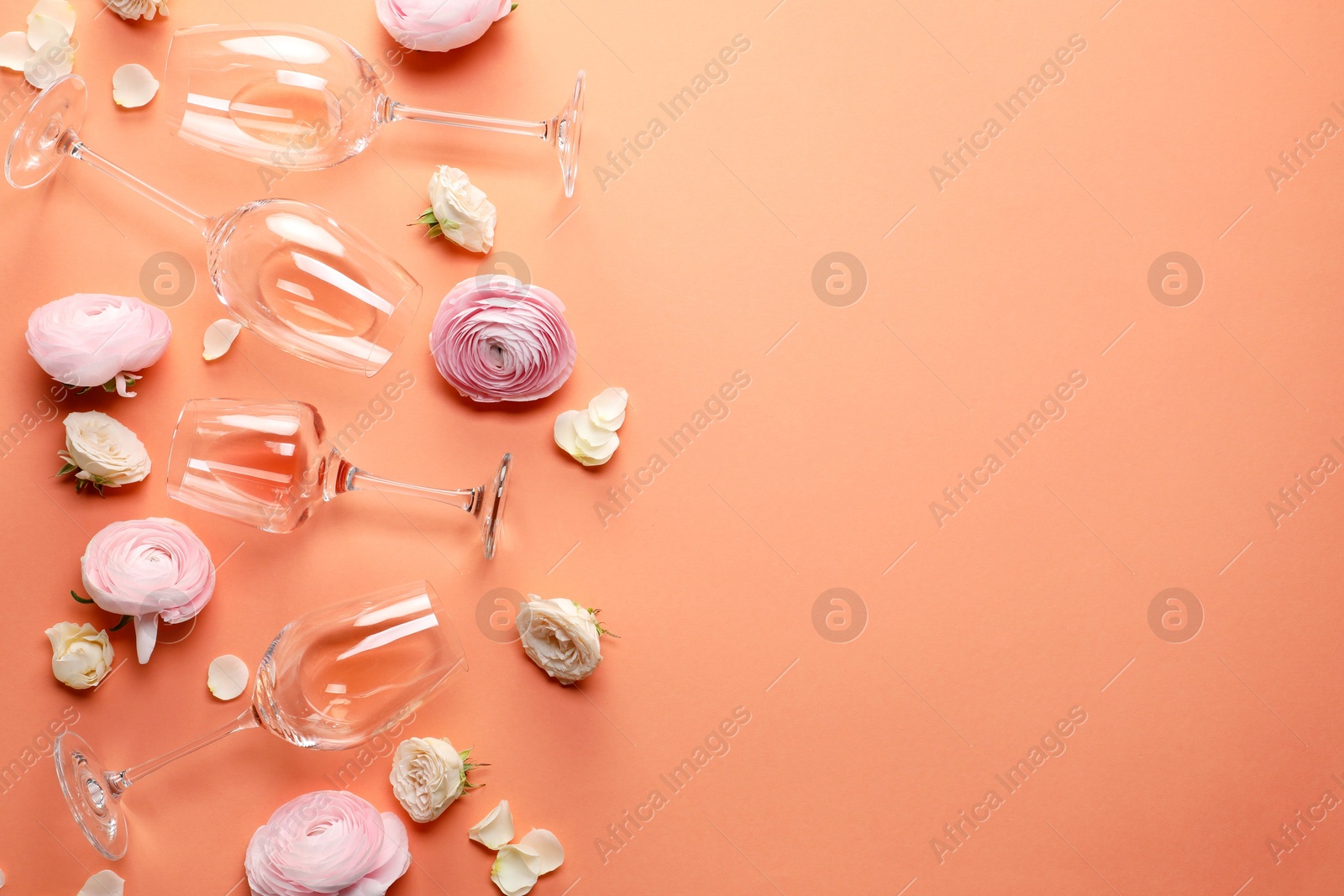 Photo of Flat lay composition with wineglasses and beautiful flowers on coral color background. Space for text