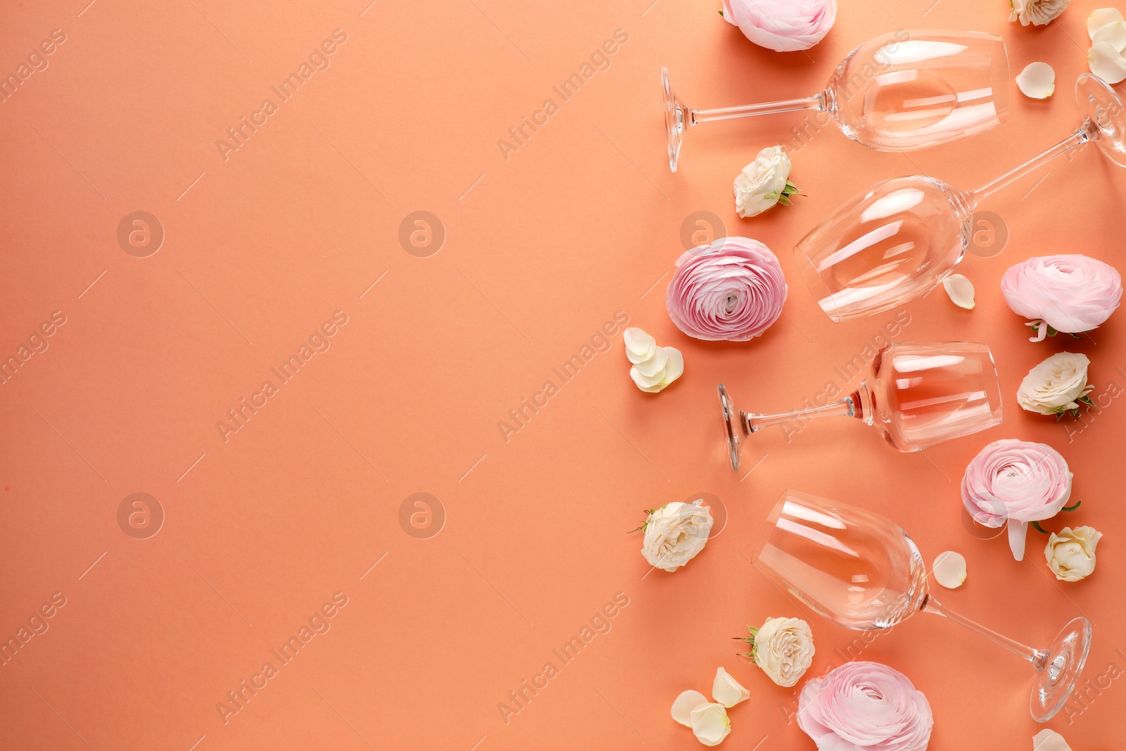 Photo of Flat lay composition with wineglasses and beautiful flowers on coral color background. Space for text