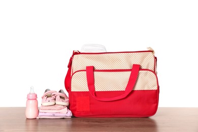 Mother's bag with baby's stuff on wooden table against white background