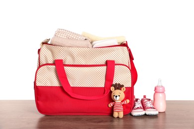 Mother's bag with baby's stuff on wooden table against white background