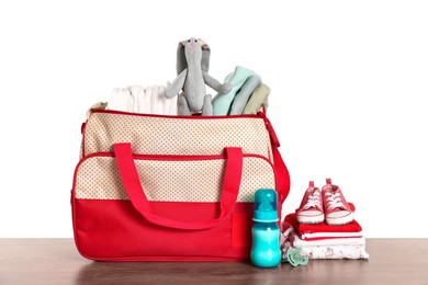 Photo of Mother's bag with baby's stuff on wooden table against white background