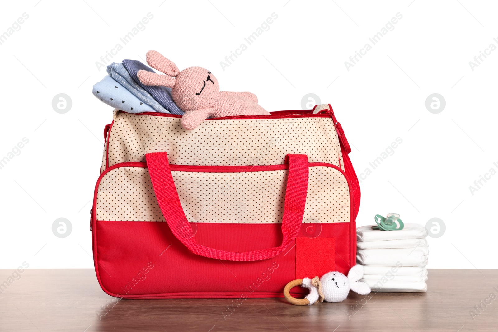 Photo of Mother's bag with baby's stuff on wooden table against white background