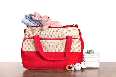 Mother's bag with baby's stuff on wooden table against white background