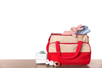 Mother's bag with baby's stuff on wooden table against white background