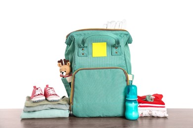 Mother's bag with baby's stuff on wooden table against white background