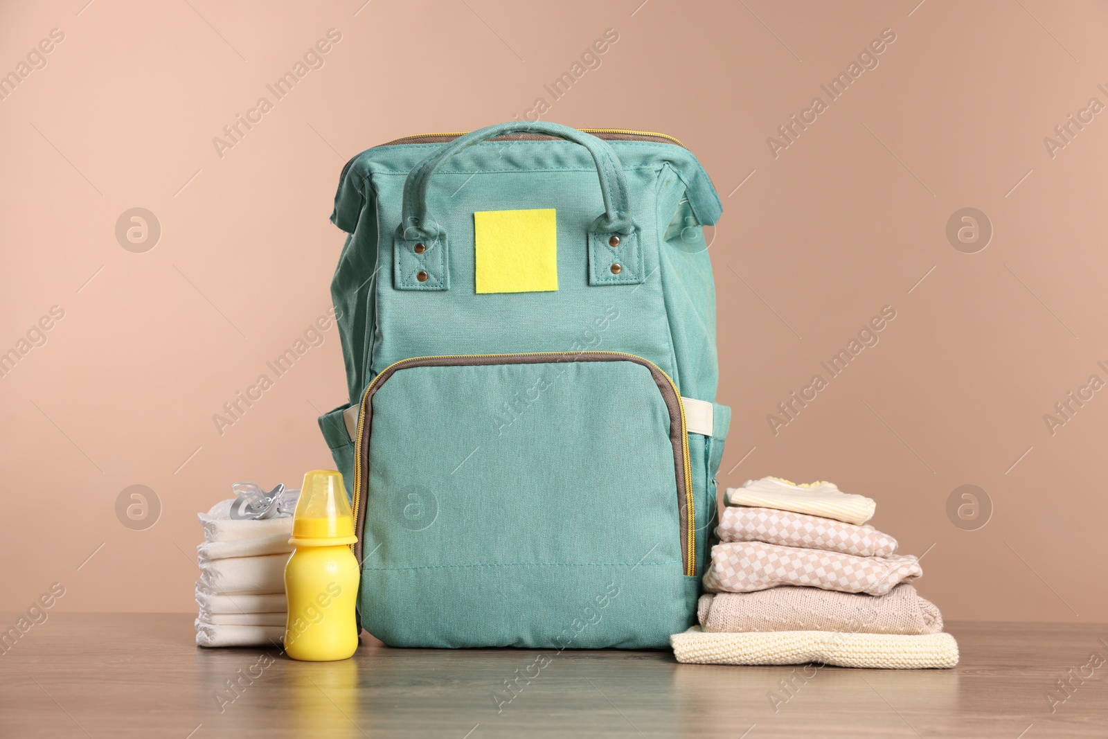 Photo of Mother's bag with baby's stuff on wooden table against beige background