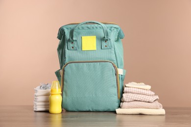 Mother's bag with baby's stuff on wooden table against beige background