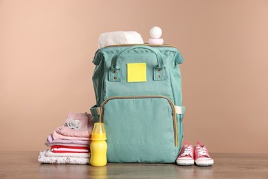 Mother's bag with baby's stuff on wooden table against beige background