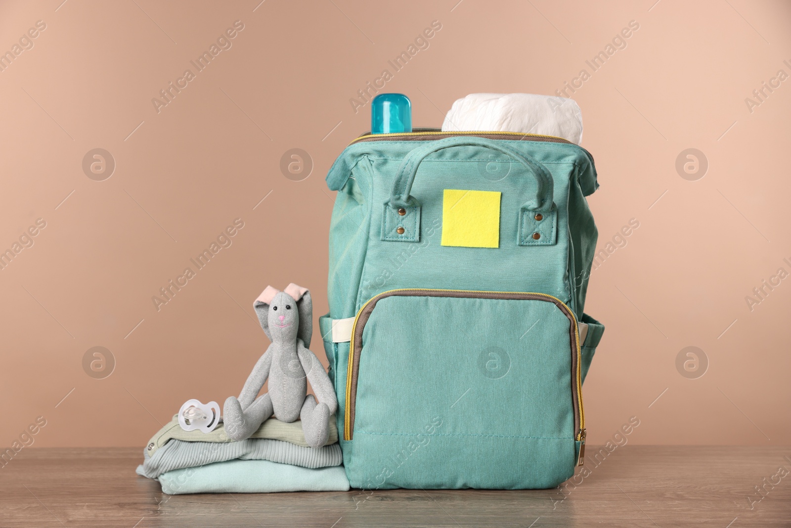 Photo of Mother's bag with baby's stuff on wooden table against beige background