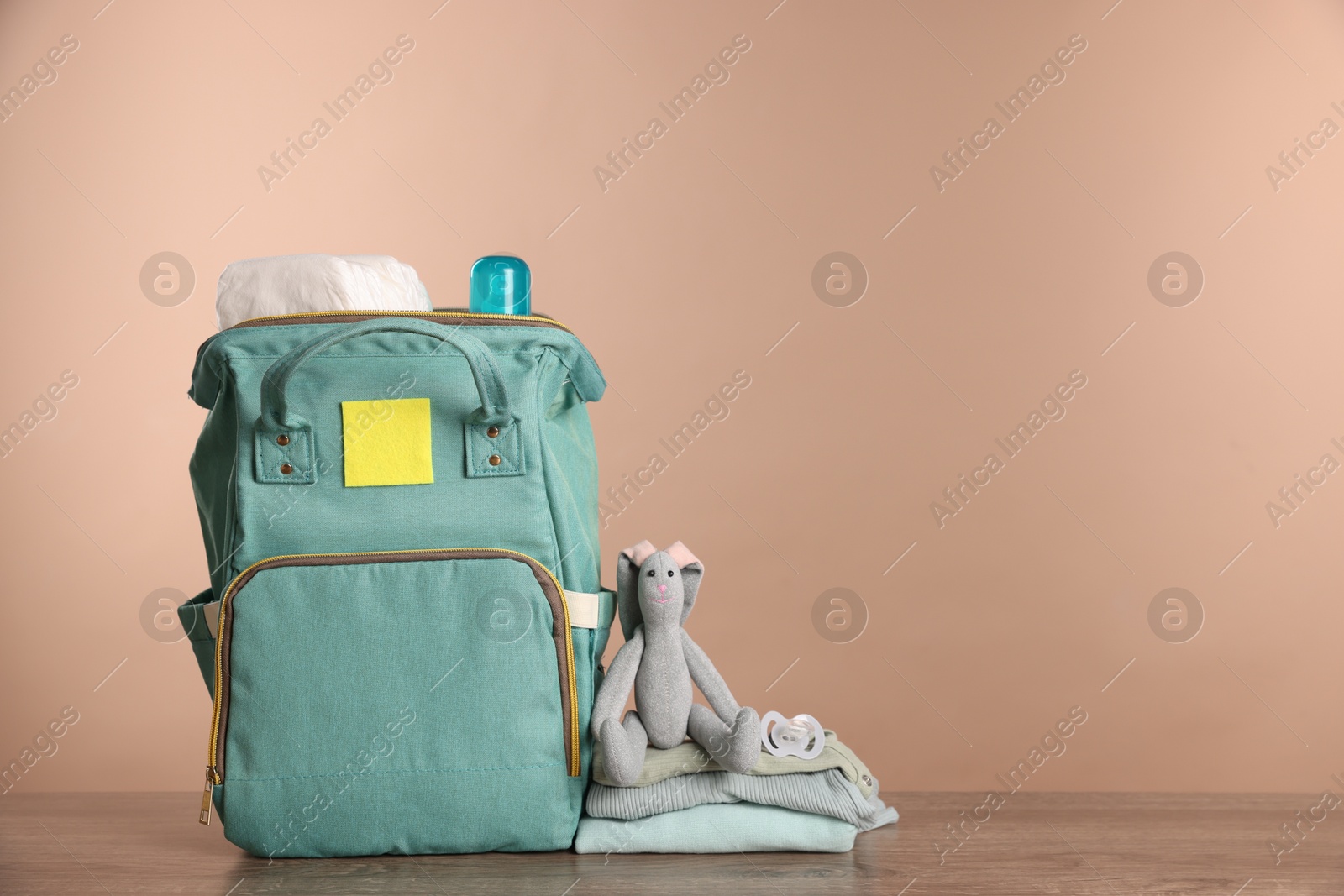 Photo of Mother's bag with baby's stuff on wooden table against beige background. Space for text