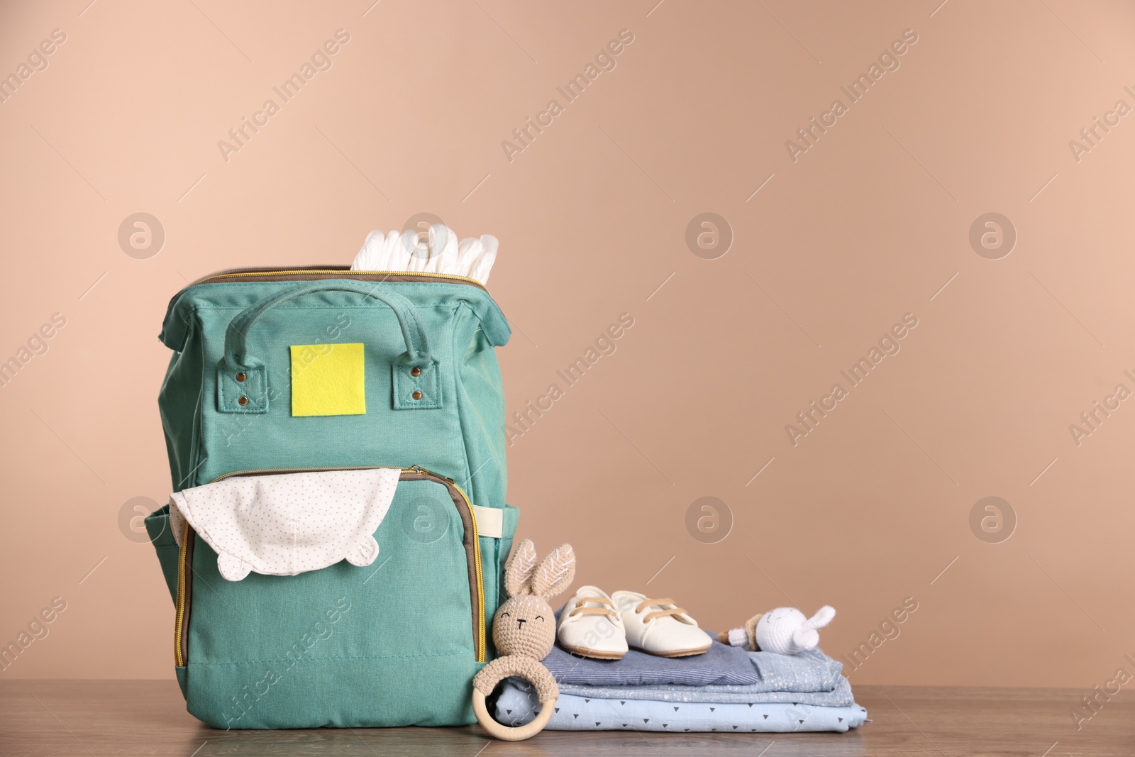 Photo of Mother's bag with baby's stuff on wooden table against beige background. Space for text