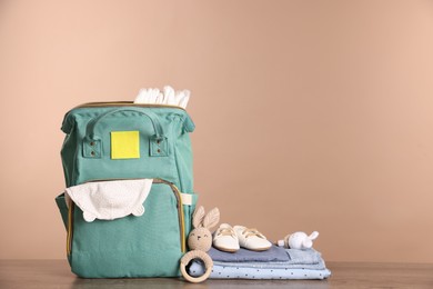 Mother's bag with baby's stuff on wooden table against beige background. Space for text